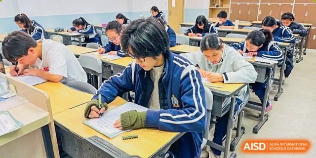 A student in a blue jacket intensely focused on writing at their desk during a class at The No.2 High School Of East China Normal University (HSEFZ).