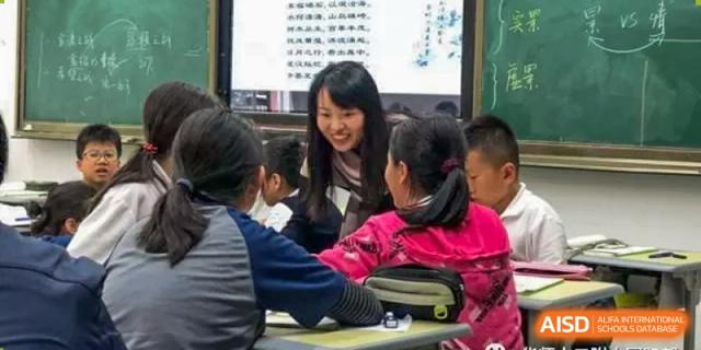 A teacher or older student smiling while assisting younger students working together around a table at The No.2 High School Of East China Normal University (HSEFZ).