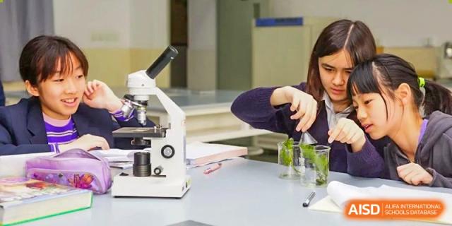 A close-up of a person's hands performing an experiment next to a microscope in a science lab at The No.2 High School Of East China Normal University (HSEFZ).