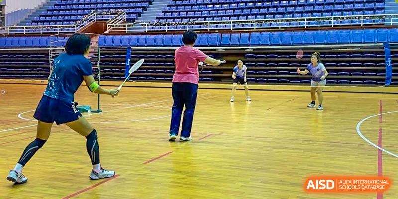 A student in a pink shirt playing badminton on the wooden court of the gymnasium at The No.2 High School Of East China Normal University (HSEFZ).