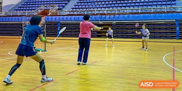 A student in a pink shirt playing badminton on the wooden court of the gymnasium at The No.2 High School Of East China Normal University (HSEFZ).