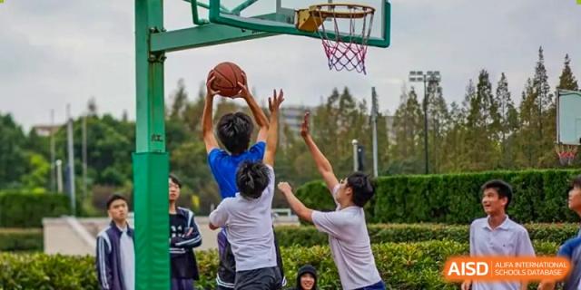 Students competing for a rebound or block during an outdoor basketball game at TheNo.2 High School Of East China Normal University (HSEFZ).