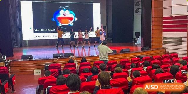 An audience of students watching a stage performance in an auditorium with red seats at The No.2 High School Of East China Normal University (HSEFZ).