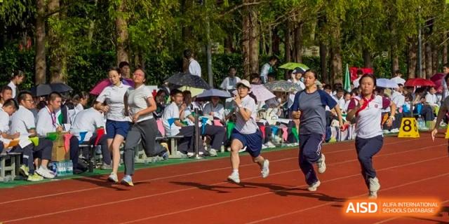 A student running on the red track during a race or sports meet, with spectators seated under umbrellas at The No.2 High School Of East China Normal University (HSEFZ).