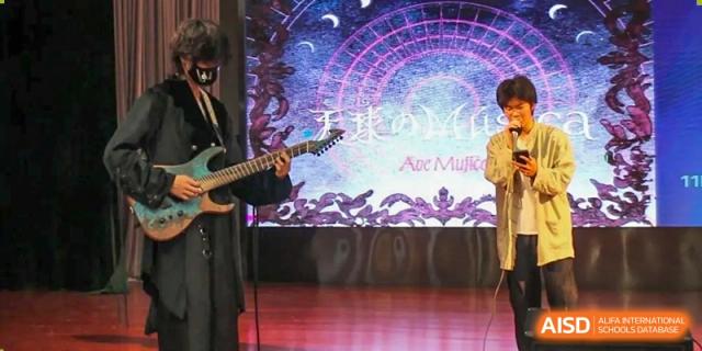 A close-up of a student playing a guitar on stage in front of a colorful digital screen at a talent show at The No.2 High School Of East China Normal University (HSEFZ).