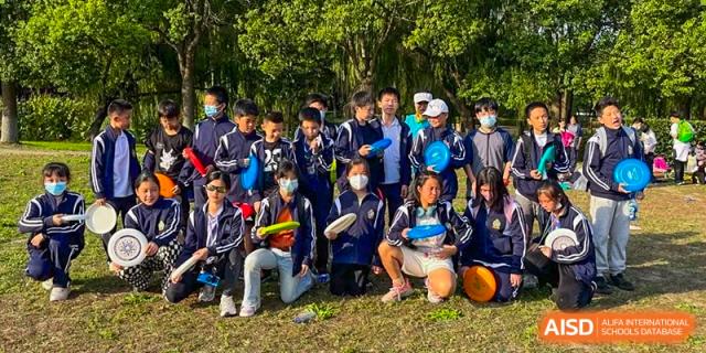 A group of students and a staff member wearing masks posing for a group photo outdoors in a wooded area at TheNo.2 High School Of East China Normal University (HSEFZ).