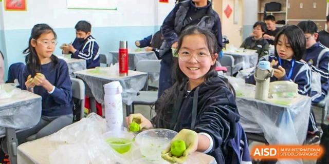 A female student smiling while holding limes or green fruit during a cooking or nutrition class at The No.2 High School Of East China Normal University (HSEFZ).