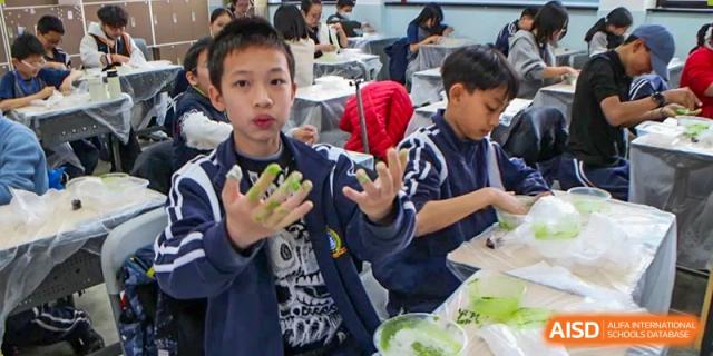 A young male student holding a red yarn ball and smiling during a hands-on activity in a class at The No.2 High School Of East China Normal University (HSEFZ).