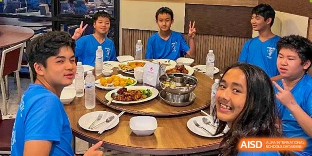 A group of students smiling and giving a peace sign while seated around a large table filled with dishes and food during a meal at The No.2 High School Of East China Normal University (HSEFZ).
