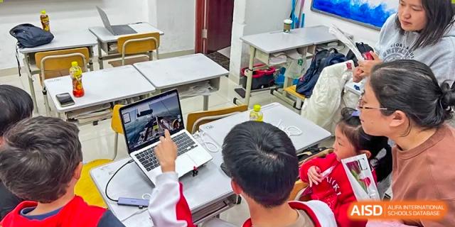 Two students in red and white uniforms are working together on a laptop at the International Curriculum Center of RDFZ.