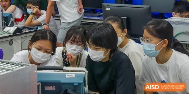 Students wearing masks are huddled together, looking at a computer screen at the International Curriculum Center of RDFZ.