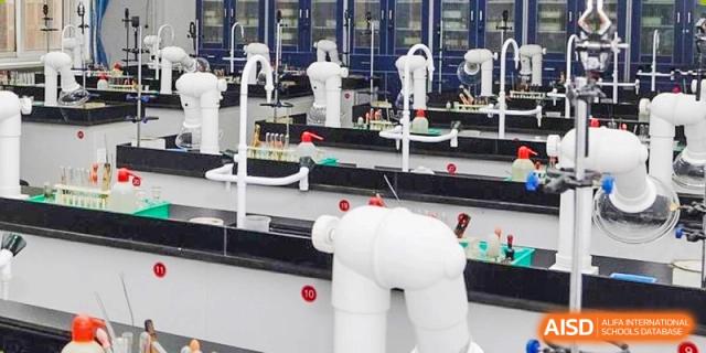 A robot is in a lab or classroom setting with students working at a desk behind it at the International Curriculum Center of RDFZ.