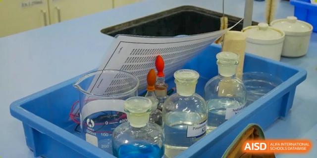 A lab notebook with writing and flasks containing blue liquid at the International Curriculum Center of RDFZ.