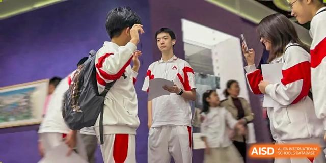 Two male students in red and white uniforms are standing and talking to each other at the International Curriculum Center of RDFZ.