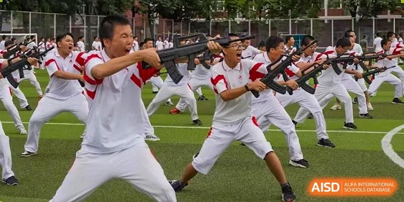 Two men in white and red sportswear are engaged in a simulated combat drill with fake rifles on a sports field at the International Curriculum Center of RDFZ.