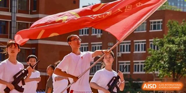 Two students in white and red uniforms are holding a large red flag on a sports field at the International Curriculum Center of RDFZ.