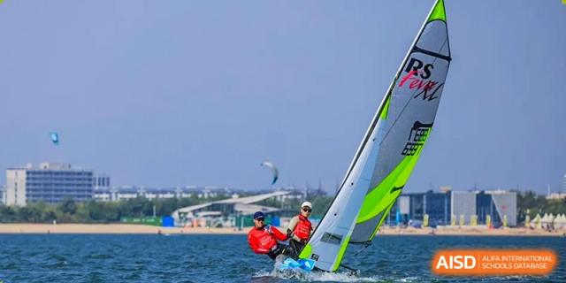A person is windsurfing on the water, with a beach and buildings in the background at the International Curriculum Center of RDFZ.