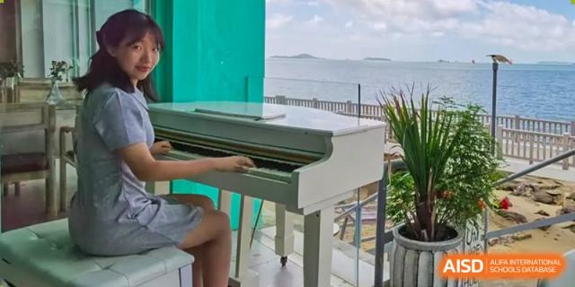 A person is seated at a white piano, with a building and the sea in the background at the International Curriculum Center of RDFZ.