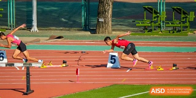 Two athletes are in the middle of a race on a running track, with one athlete jumping over a hurdle at the International Curriculum Center of RDFZ.