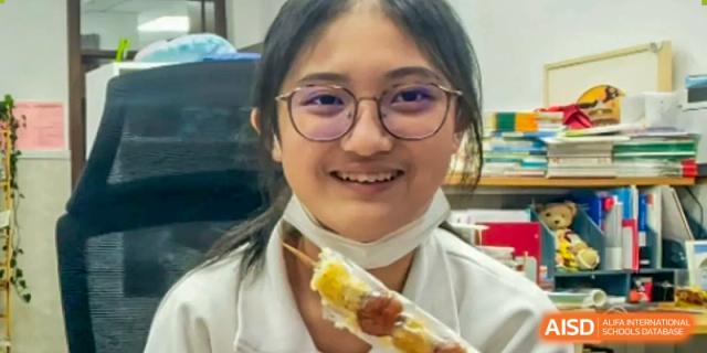 A female student in a white uniform is smiling and holding a corn on the cob at the International Curriculum Center of RDFZ.