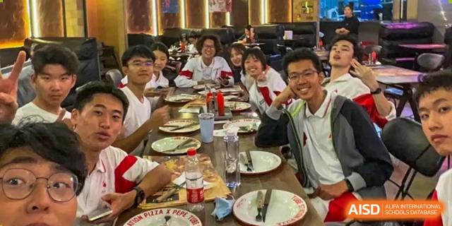 A group of students in red and white uniforms are seated at a table, smiling for a group photo at a restaurant at the International Curriculum Center of RDFZ.