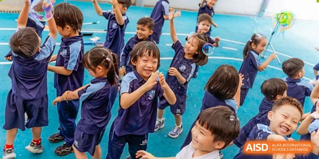 A group of young students from ISA Science City International School is playing and laughing together. One student in the foreground is smiling widely with a soap bubble near his face.