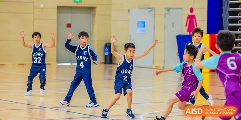 A young student from ISA Science City International School, wearing a basketball jersey, is posing playfully on the indoor court.