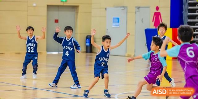 A young student from ISA Science City International School, wearing a basketball jersey, is posing playfully on the indoor court.