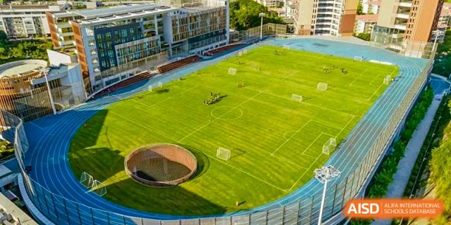 An aerial view of a sports field at ISA Science City International School, with a soccer game in progress.