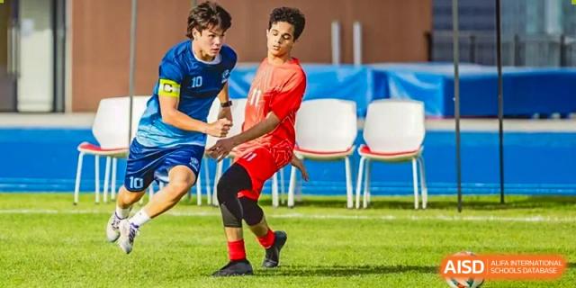 A student from ISA Science City International School wearing a red jersey is playing soccer on a grass field.
