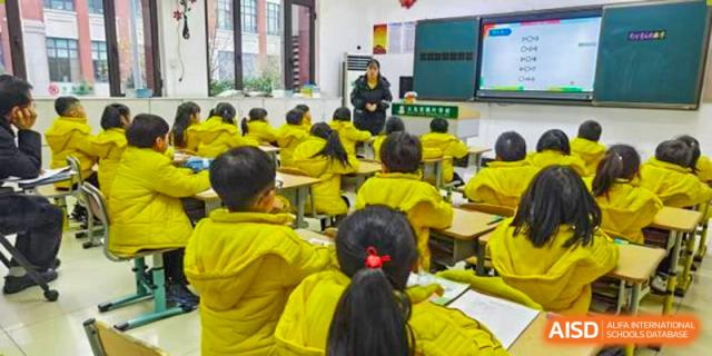 A large class of young students wearing bright yellow shirts and seated at desks during a lesson at Maple Leaf Foreign Nationals School-Yiwu.