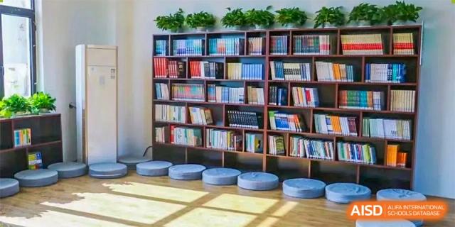 A floor-to-ceiling bookshelf filled with books, with round cushioned seats in front of it in a library area at Maple Leaf Foreign Nationals School-Yiwu.