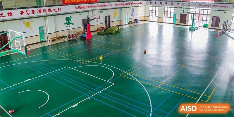 Empty green indoor basketball court with yellow and blue lines, suitable for sports at Maple Leaf Foreign Nationals School-Yiwu.