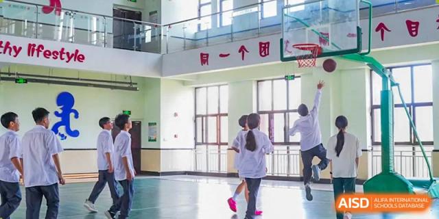 Students playing basketball indoors near a hoop and a second-floor glass railing at Maple Leaf Foreign Nationals School-Yiwu.