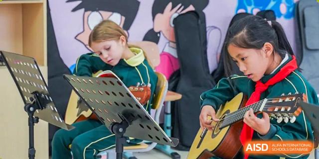 A young female student plays a musical instrument, reading sheet music on a stand while another student plays a guitar at Maple Leaf Foreign Nationals School-Yiwu.