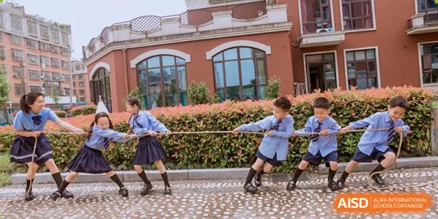 Students in school uniforms participating in a tug-of-war game outside in front of a red brick building at Maple Leaf Foreign Nationals School-Yiwu.