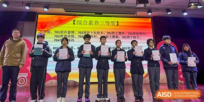 Students in dark uniforms holding up certificates of achievement on a stage with a banner displaying Chinese text and a "Second Prize" designation at Maple Leaf Foreign Nationals School-Yiwu.