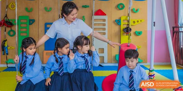 Three young female students in blue uniforms interacting with an adult in a brightly colored indoor play area at Maple Leaf Foreign Nationals School-Yiwu.