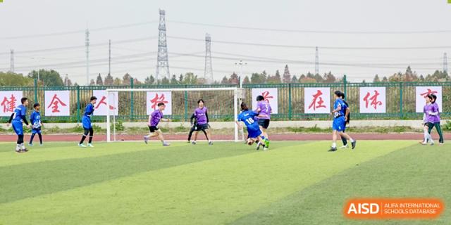 Students in purple and blue sports uniforms playing soccer on a bright green outdoor field at Maple Leaf Foreign Nationals School-Yiwu.