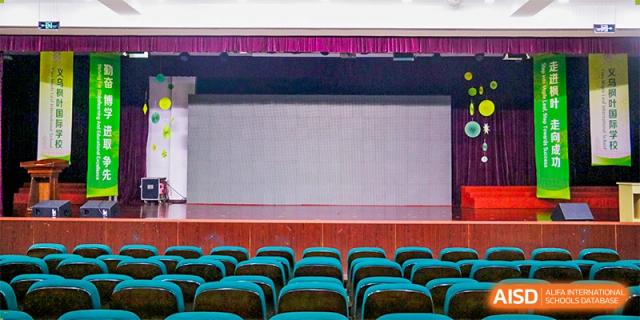 An empty auditorium stage featuring a large white projection screen and rows of teal-colored seats at Maple Leaf Foreign Nationals School-Yiwu.