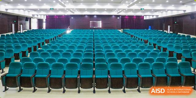 A view of the empty school auditorium with numerous rows of dark teal seats and bright ceiling lighting at Maple Leaf Foreign Nationals School-Yiwu.