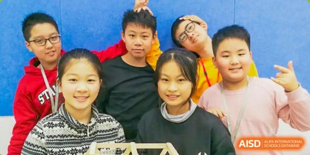 A group of NANJING THOMAS SCHOOL students are smiling while working on a project.