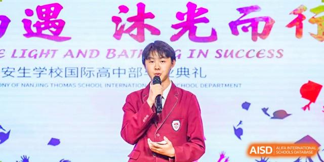 A NANJING THOMAS SCHOOL student in a red uniform is giving a speech on a stage.