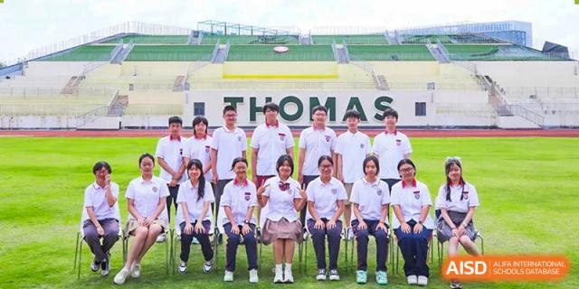 A group of NANJING THOMAS SCHOOL students and staff are posing for a photo on a sports field.