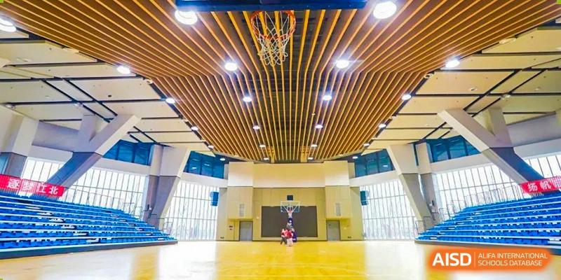 A NANJING THOMAS SCHOOL student is dribbling a basketball in a well-lit indoor gymnasium.