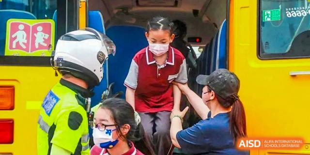 A young NANJING THOMAS SCHOOL student in a face mask is getting off a bus with the help of an adult.