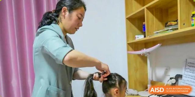 An adult is helping a young NANJING THOMAS SCHOOL student by tying her hair.