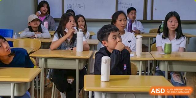 A boy with glasses sitting at a desk in a classroom, looking to his left, at the Qingdao Amerasia International School.