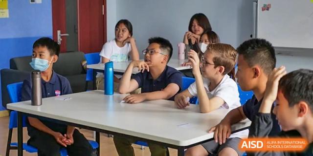 A group of students sitting at a table in a classroom, listening attentively to a lesson at the Qingdao Amerasia International School.
