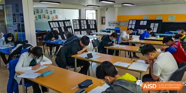 A group of students focused on their work at desks in a classroom or library at the Qingdao Amerasia International School.